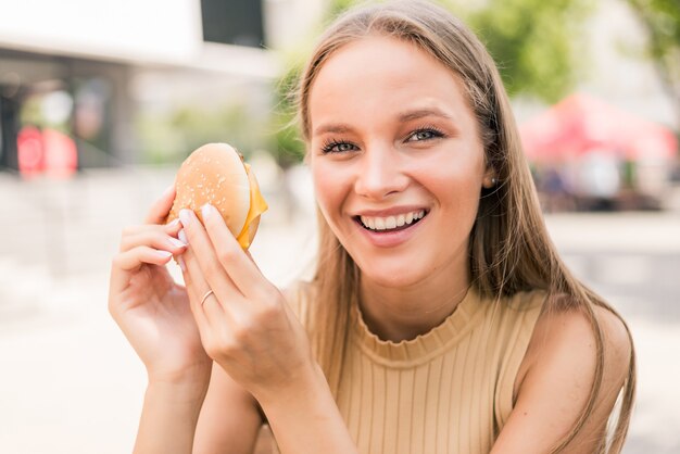 Mujer bonita joven comiendo hamburguesas en street cafe