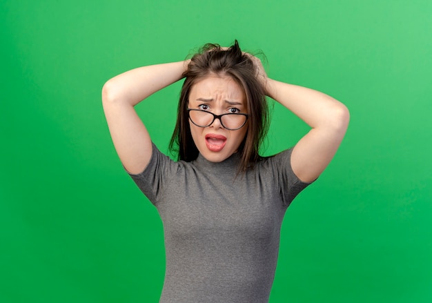 Foto gratuita mujer bonita joven descontenta con gafas poniendo las manos en la cabeza aislada sobre fondo verde