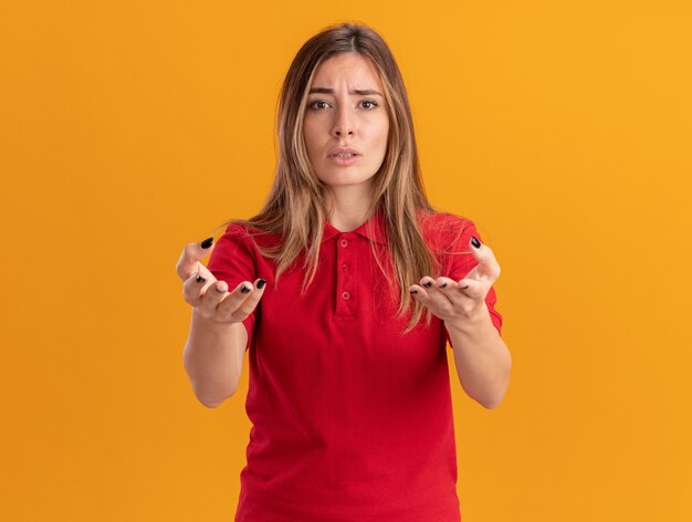 Mujer bonita joven despistada apunta al frente con las manos aisladas en la pared naranja