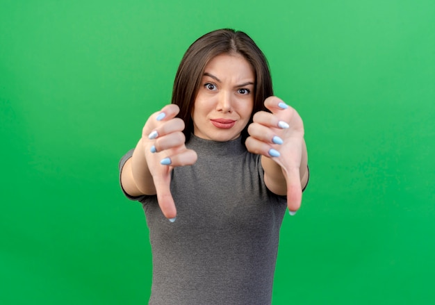 Mujer bonita joven disgustada mostrando los pulgares hacia abajo aislado sobre fondo verde con espacio de copia