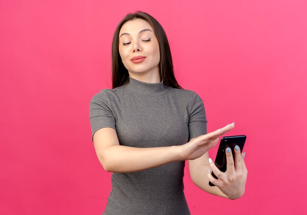 Mujer bonita joven disgustada sosteniendo mirando el teléfono móvil y gesticulando no aislado sobre fondo rosa con espacio de copia