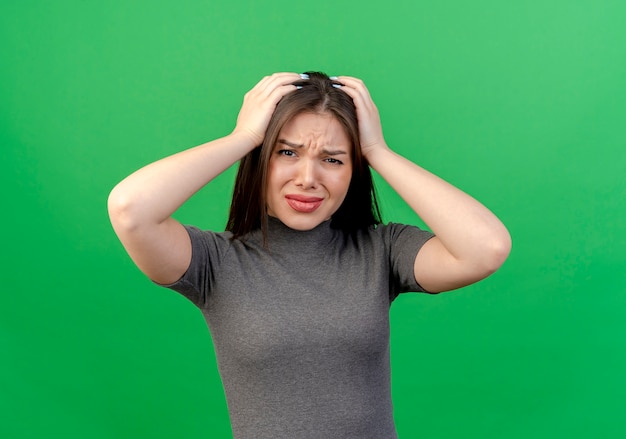 Mujer bonita joven disgustada sosteniendo su cabeza aislada sobre fondo verde