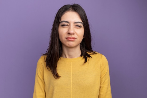 Mujer bonita joven dudosa mirando al frente frunciendo los ojos aislados en la pared púrpura con espacio de copia