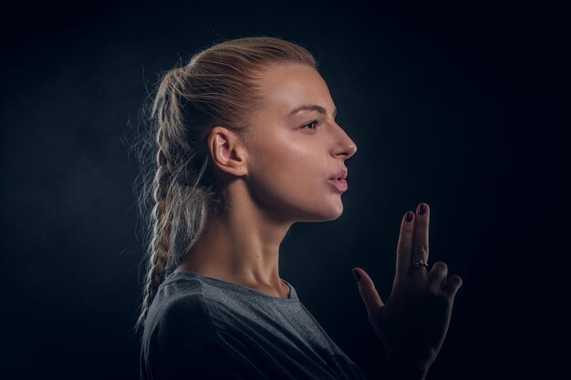 Una mujer bonita joven está mostrando un arma con los dedos en un estudio fotográfico oscuro.