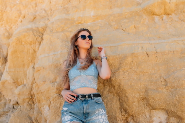 Mujer bonita joven en gafas de sol en la playa rocosa