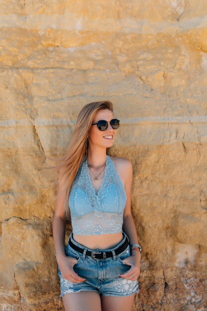 Mujer bonita joven en gafas de sol en la playa rocosa