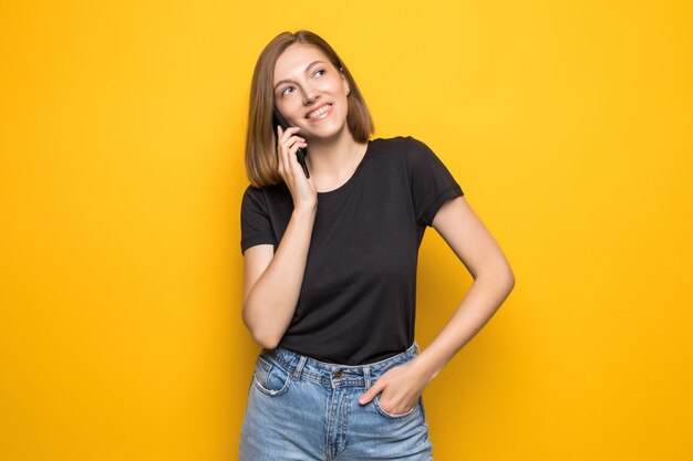 Mujer bonita joven hablando por teléfono celular sobre pared amarilla