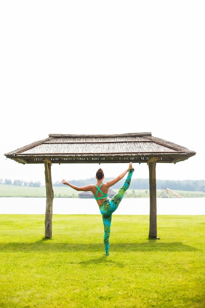 Mujer bonita joven haciendo yoga en el parque de la mañana cerca del lago