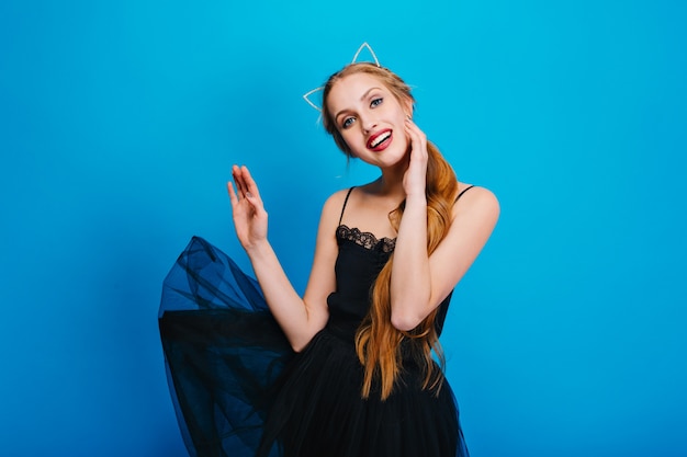 Mujer bonita joven con hermosa sonrisa, vestido negro ondeando, posando. Tiene el pelo largo, diadema con orejas de gato, bonito maquillaje con pintalabios rojo.