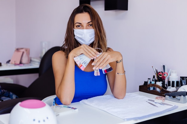 Mujer bonita joven en máscara médica protectora en salón de belleza de uñas con increíble luz suave natural