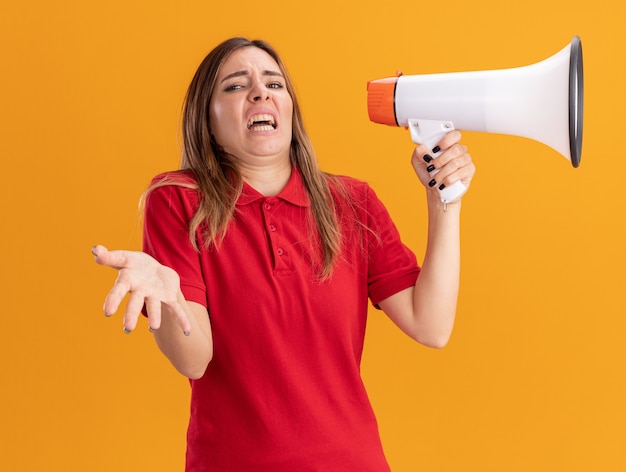 Foto gratuita mujer bonita joven molesta sostiene altavoz y apunta al frente con la mano aislada en la pared naranja