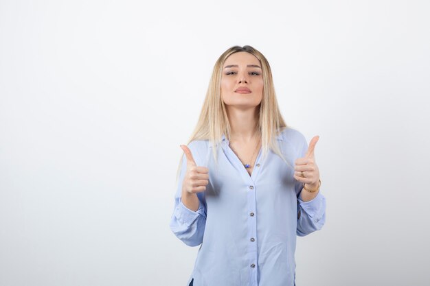 Mujer bonita joven de pie y dando pulgar hacia arriba en la pared blanca