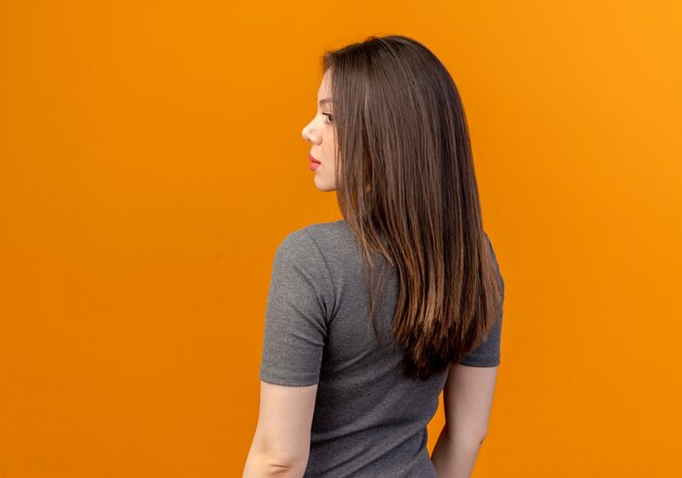 Mujer bonita joven de pie detrás de la vista y mirando al lado aislado sobre fondo naranja con espacio de copia