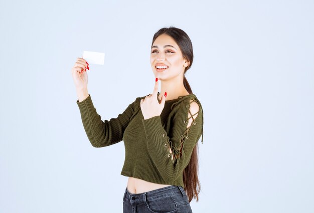 Mujer bonita joven de pie con tarjeta de visita en blanco sobre fondo blanco.