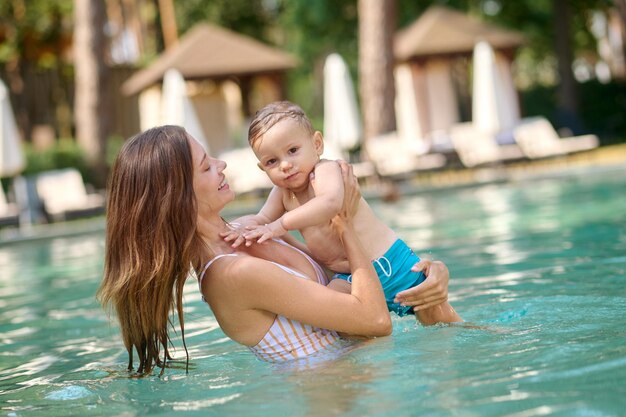 Mujer bonita joven en una piscina con su bebé