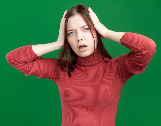 Mujer bonita joven preocupada mirando al frente manteniendo las manos en la cabeza aislada en la pared verde