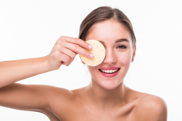 Mujer bonita joven que aplica colorete en su cara con el soplo de polvo aislado en la pared blanca