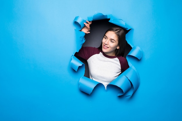 Mujer bonita joven que mira a través del agujero azul en la pared de papel.