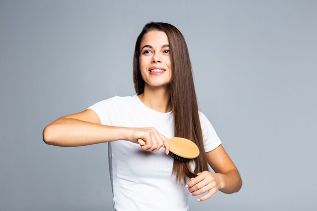 Mujer bonita joven que se peina el pelo aislado en blanco