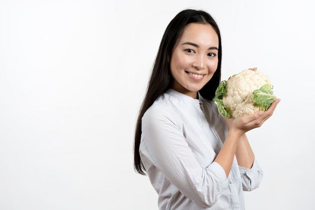 Mujer bonita joven que sostiene la coliflor fresca delante del fondo blanco