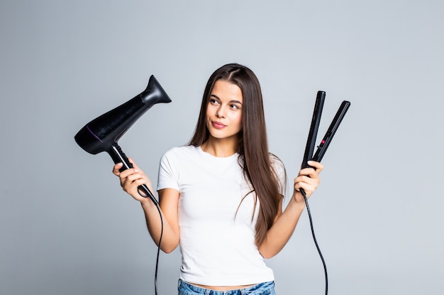 Mujer bonita joven que sostiene el secador de pelo y alisar aislado en blanco