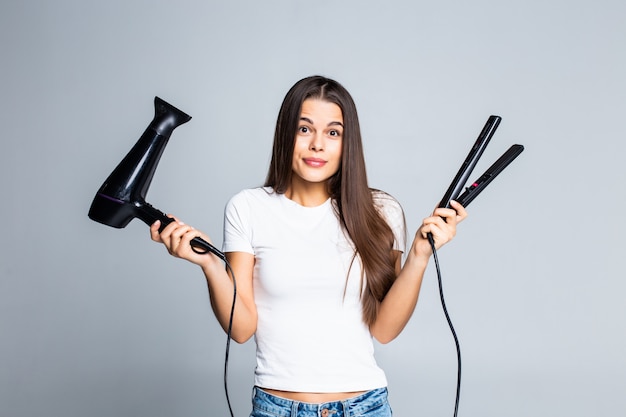 Mujer bonita joven que sostiene el secador de pelo y alisar aislado en blanco