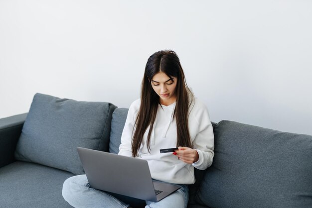 Mujer bonita joven que trabaja con computadora portátil y tarjeta de crédito en casa