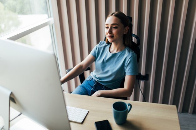 Mujer bonita joven que trabaja en el pc en la oficina en casa