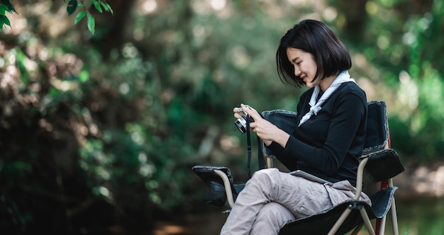 Mujer bonita joven que usa una cámara digital para tomar una foto de la hermosa naturaleza mientras acampa en el bosque con espacio de copia de felicidad