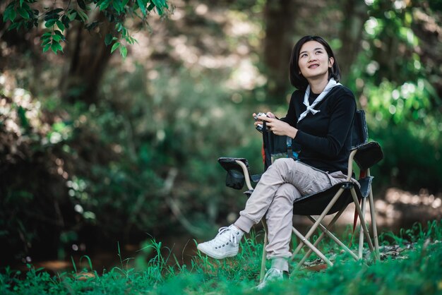 Mujer bonita joven que usa una cámara digital para tomar una foto de la hermosa naturaleza mientras acampa en el bosque con espacio de copia de felicidad