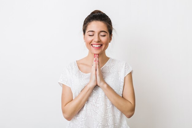 Mujer bonita joven rezando con una sonrisa, pidiendo un deseo, ojos cerrados,