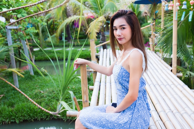 Mujer bonita joven sentada en el puente de bambú en jardín