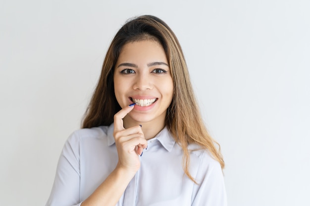 Mujer bonita joven sonriente que mira la cámara y que toca el labio