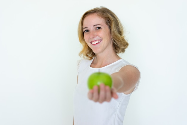 Mujer bonita joven sonriente que ofrece la manzana verde borrosa