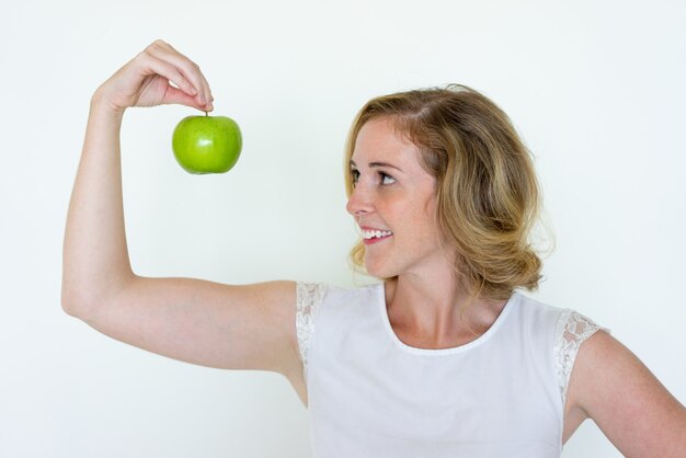 Mujer bonita joven sonriente que sostiene la manzana verde con los dedos