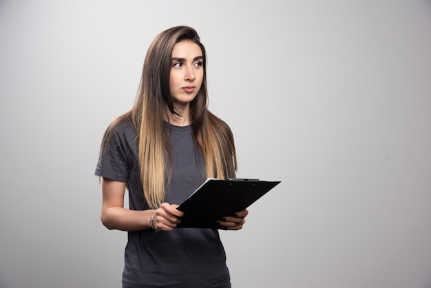 Mujer bonita joven sosteniendo un portapapeles sobre un fondo gris.