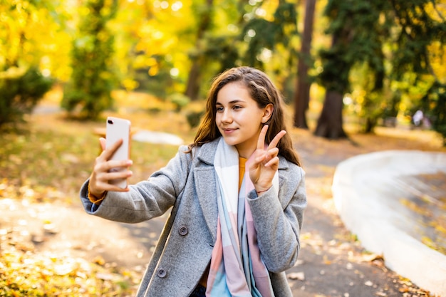 Mujer bonita joven toma el teléfono por teléfono en el parque otoño