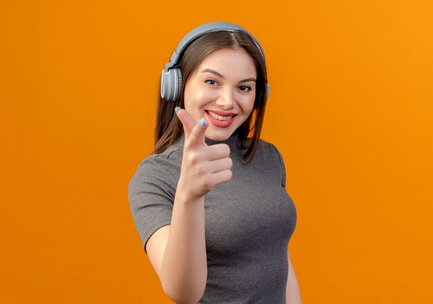 Mujer bonita joven usando audífonos para escuchar música aislado en naranja