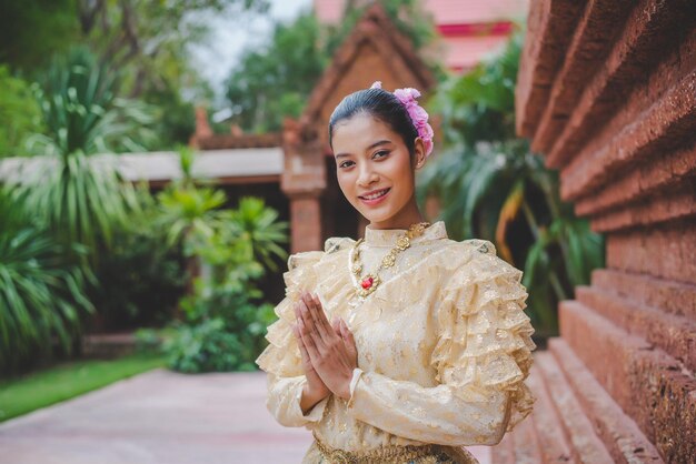 Mujer bonita joven vestida con hermosos trajes tailandeses de pie con las manos cruzadas con respeto en el templo en el festival Songkran Día de la Familia del Año Nuevo Tailandés en abril