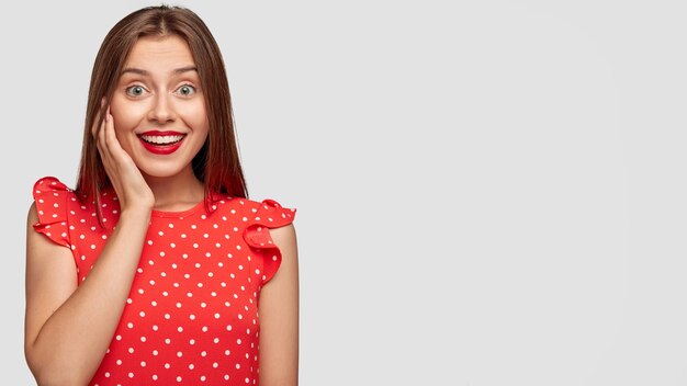 Mujer bonita con lápiz labial rojo posando contra la pared blanca