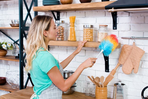 Mujer bonita limpieza estante de cocina con plumero suave