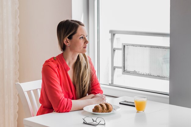 Mujer bonita mirando por la ventana durante el desayuno