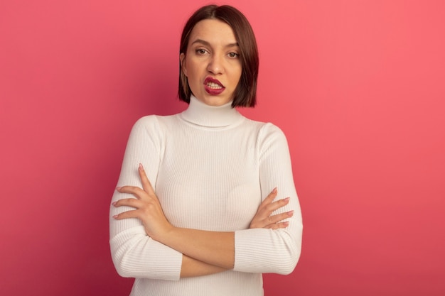 Mujer bonita molesta de pie con los brazos cruzados aislado en la pared rosa