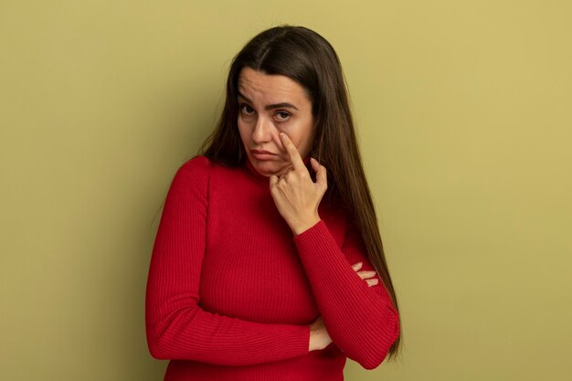 Mujer bonita molesta tira hacia abajo el párpado mirando al frente aislado en la pared verde oliva