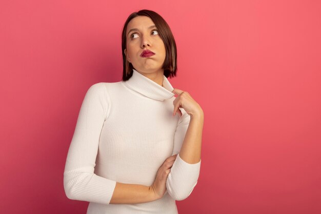 Mujer bonita molesta tira del cuello mirando al lado aislado en la pared rosa