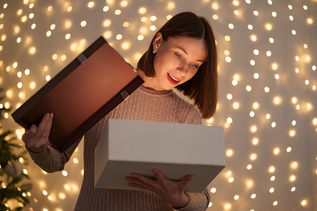 Mujer bonita morena abre un adorable regalo con luces