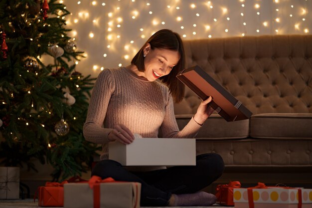 Mujer bonita morena abre un adorable regalo con luces