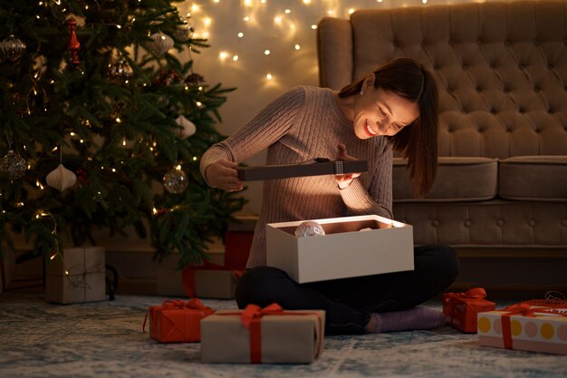 Mujer bonita morena abre un adorable regalo con luces