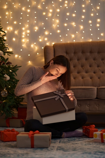 Mujer bonita morena abre un adorable regalo con luces