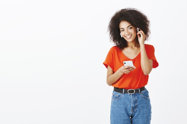 Mujer bonita con peinado afro posando con su teléfono inteligente y auriculares en el estudio